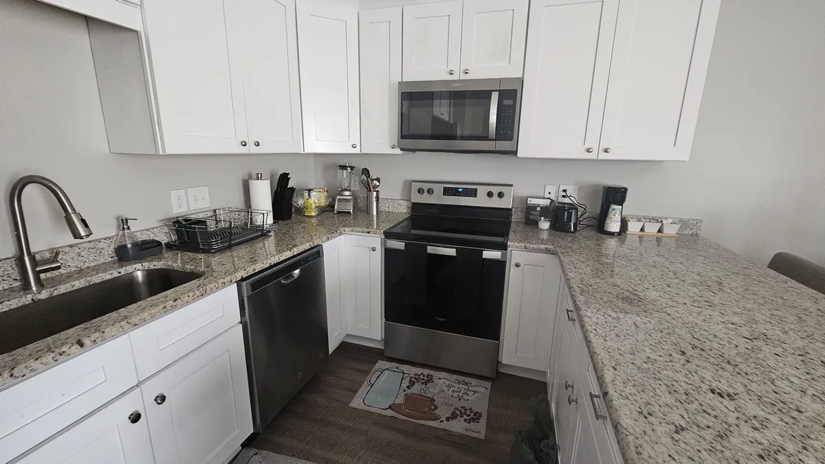 An inviting interior shot of a kitchen and dining area, with granite countertops, stainless steel appliances, and spacious white cabinetry. The setting is lively, hinting at a group preparing food, sharing recipes, or gathering for a family brunch. The scene exudes warmth and togetherness, emphasizing the communal aspect of the kitchen and dining spaces.