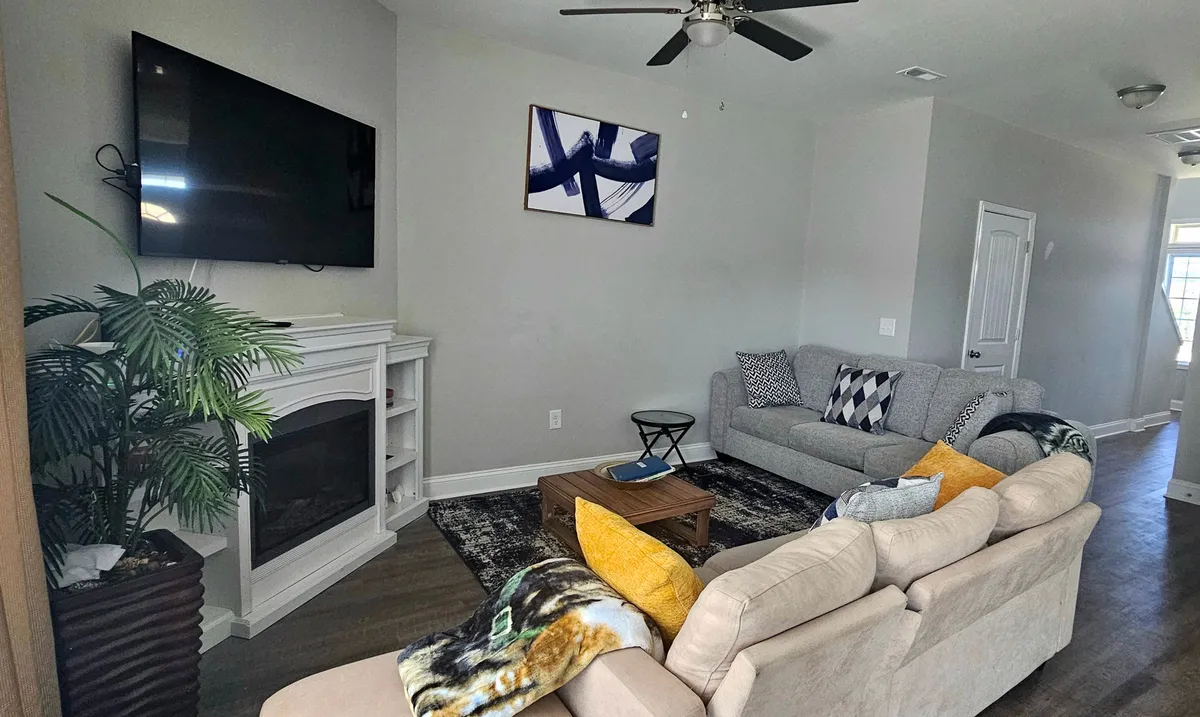 A stylish, inviting living area centered around a soft sofa, mounted television, eye-catching artwork, and a fireplace. The setup encourages group activities like watching movies or engaging in conversation, and the decor is both cozy and contemporary.