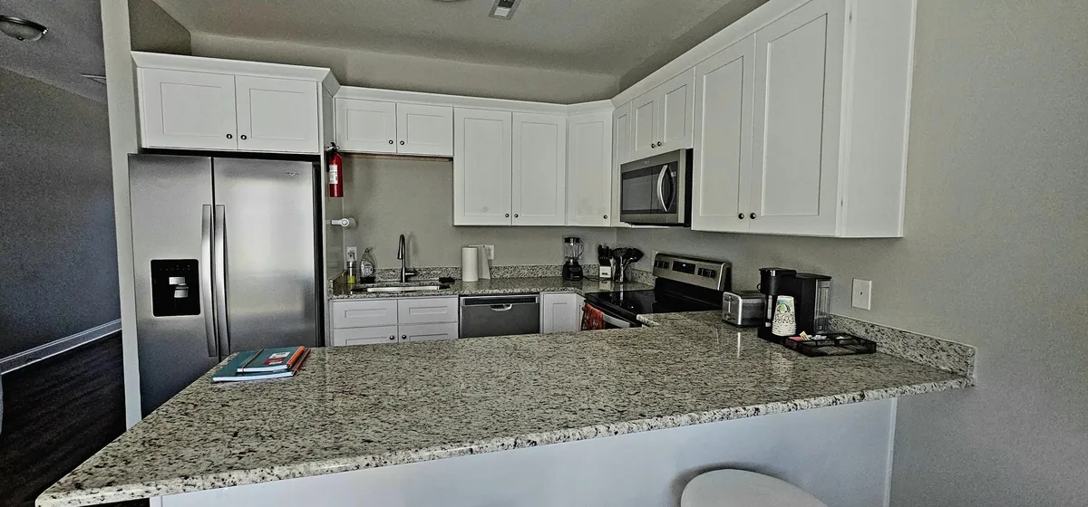 A welcoming kitchen scene featuring sleek granite countertops, stainless steel appliances, and crisp white cabinetry. The open layout suggests a space perfect for both casual breakfasts and festive group dinners. Warm ambient lighting hints at lively conversation and shared moments, with subtle cues to activities like baking, cooking, and entertaining.