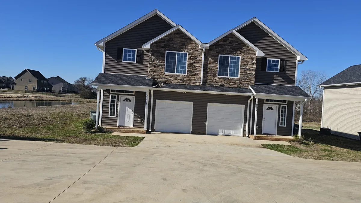 This exterior image features the duplex facade with stone accents, large windows, and a spacious driveway, immediately conveying the property's welcoming appearance and highlighting the independent entrances. The presence of the driveway visually emphasizes the availability of free on-site parking, and the design of the building supports the concept of privacy within a shared structure.